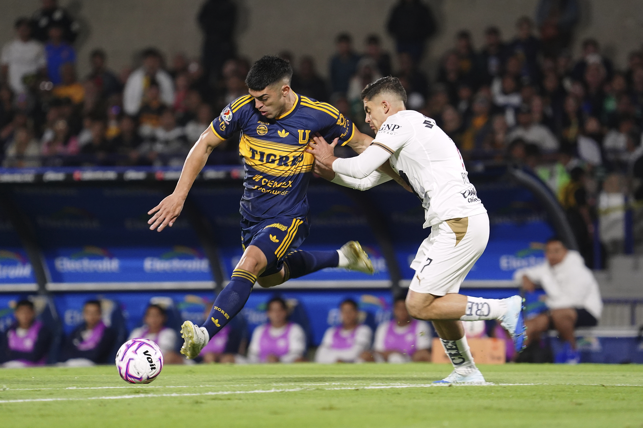 Jugador de Tigres conduce el balón ante la marca de un jugador de Pumas en el Estadio Olímpico Universitario